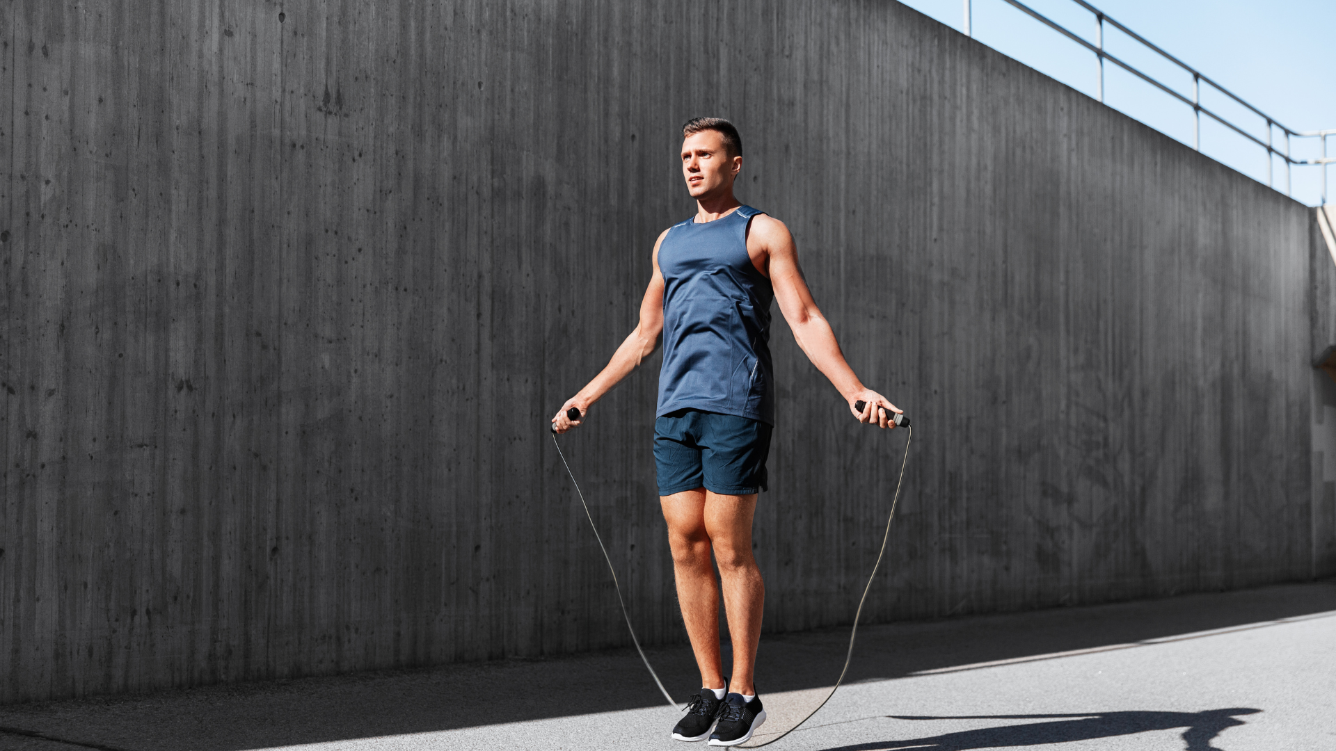 An active man wearing workout attire jumps rope with a focused expression, demonstrating high intensity and athleticism.