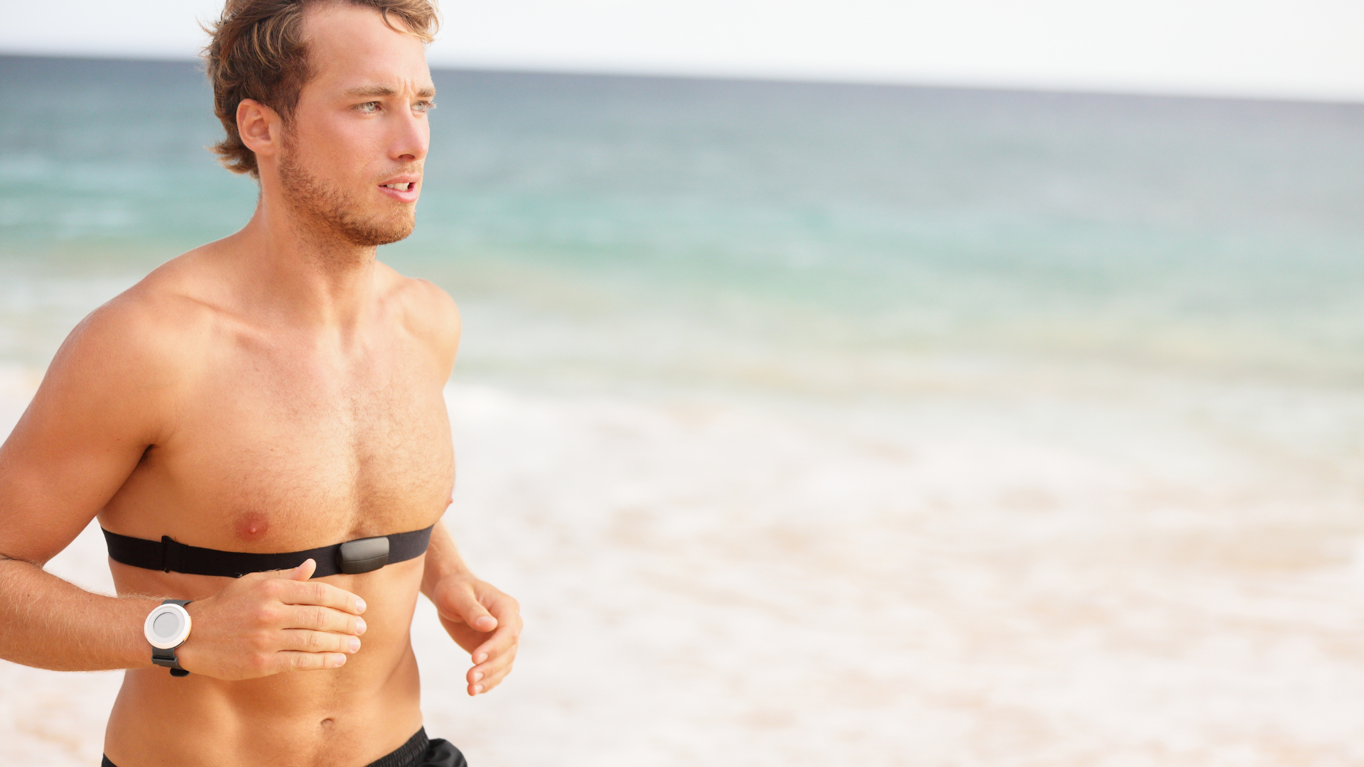 A man running on the beach wearing a heart-rate monitor.