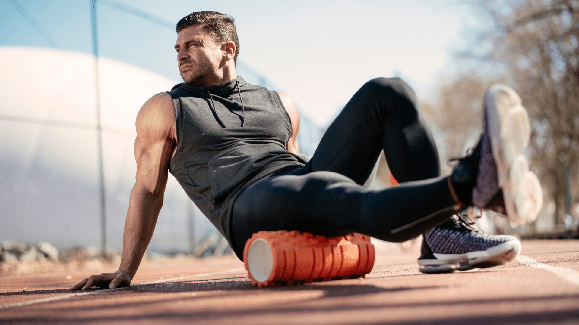 An energetic man with a determined look on his face, clad in athletic attire, is engaged in a dynamic stretching routine.